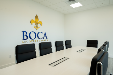 conference room at the Boca Recovery Center addiction treatment facility, featuring a long meeting table, black leather chairs, and the official Boca Recovery Center logo on the wall.