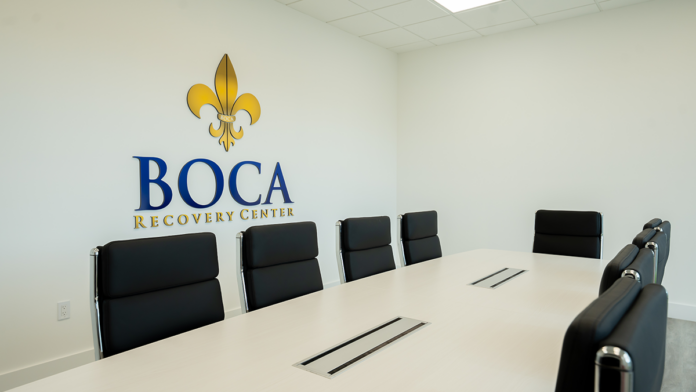 conference room at the Boca Recovery Center addiction treatment facility, featuring a long meeting table, black leather chairs, and the official Boca Recovery Center logo on the wall.