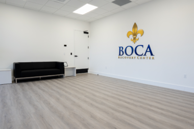 The modern waiting area at Boca Recovery Center featuring a black sofa and the clinic's logo.