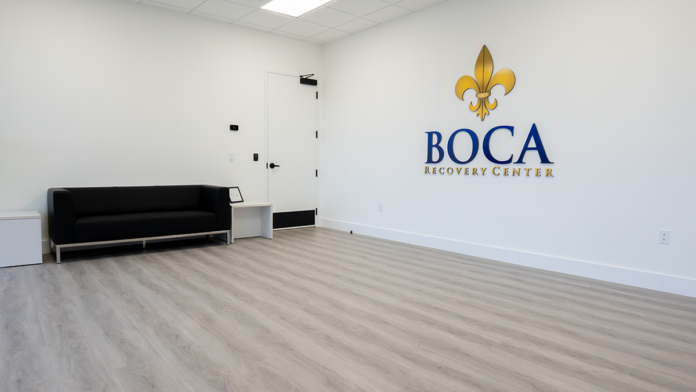 The modern waiting area at Boca Recovery Center featuring a black sofa and the clinic's logo.