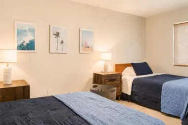 Shared bedroom at Recovery Beach with two beds, nightstands, and surf-themed wall art