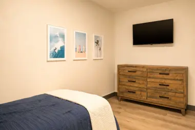 Bedroom at Recovery Beach with a wood dresser, wall-mounted TV, and surf-themed art prints