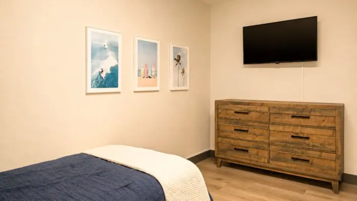 Bedroom at Recovery Beach with a wood dresser, wall-mounted TV, and surf-themed art prints