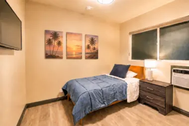 Bedroom at Recovery Beach with a single bed, nightstand, and palm tree sunset artwork