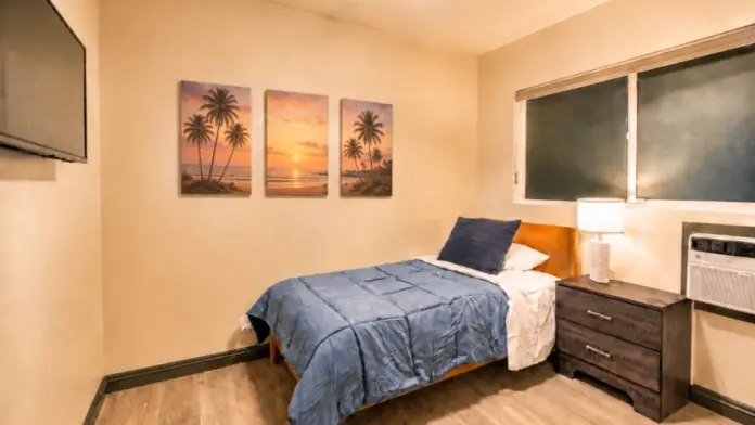 Bedroom at Recovery Beach with a single bed, nightstand, and palm tree sunset artwork