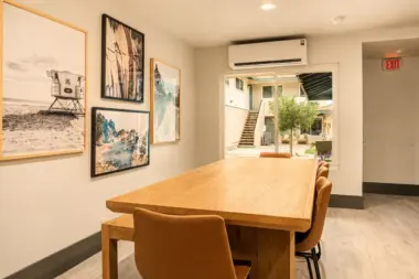 Dining room at Recovery Beach with wood table seating, gallery wall art, and sliding door view of the courtyard