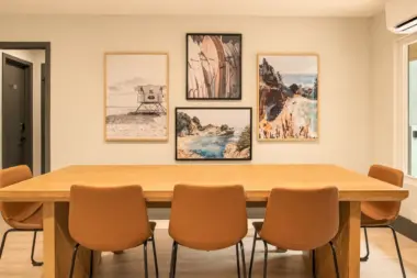Dining room at Recovery Beach with a long wood table, leather chairs, and a gallery wall of coastal artwork
