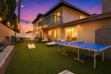 Backyard game area at Recovery Beach at dusk with a ping pong table, cornhole boards, and string lights