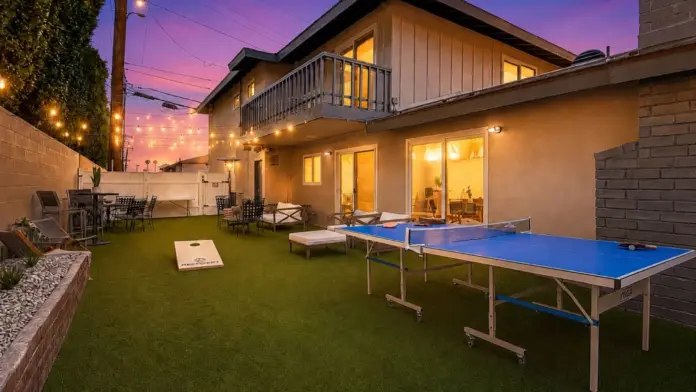 Backyard game area at Recovery Beach at dusk with a ping pong table, cornhole boards, and string lights
