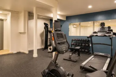 On-site fitness room at Recovery Beach with a treadmill, exercise bike, free weights, and mirrored wall