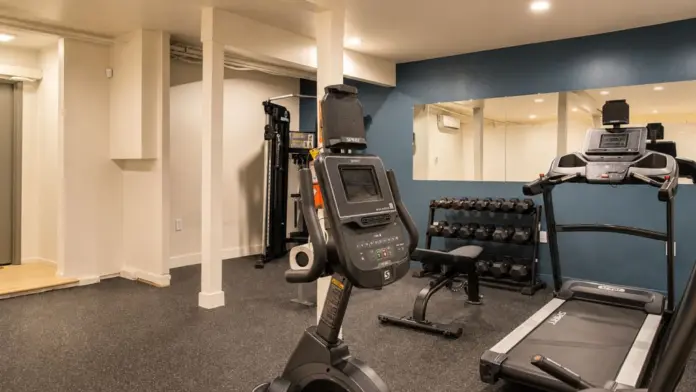 On-site fitness room at Recovery Beach with a treadmill, exercise bike, free weights, and mirrored wall