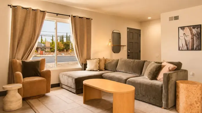 Living room at Recovery Beach with a gray sectional sofa, wood coffee table, and street-facing window