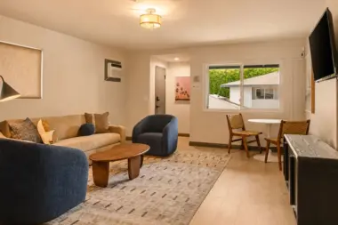 Living suite at Recovery Beach with navy accent chairs, a beige sofa, dining table, and TV