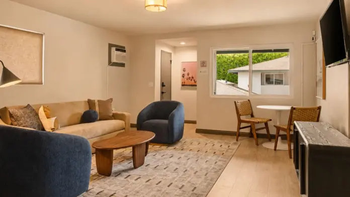 Living suite at Recovery Beach with navy accent chairs, a beige sofa, dining table, and TV