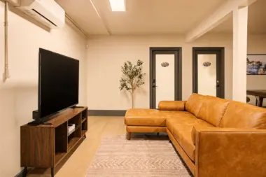 Common lounge at Recovery Beach with a tan leather sectional sofa and wall-mounted TV