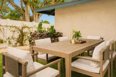 Outdoor dining table with wicker-back chairs on the patio at Recovery Beach, surrounded by greenery