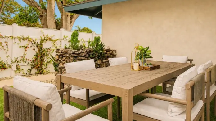 Outdoor dining table with wicker-back chairs on the patio at Recovery Beach, surrounded by greenery