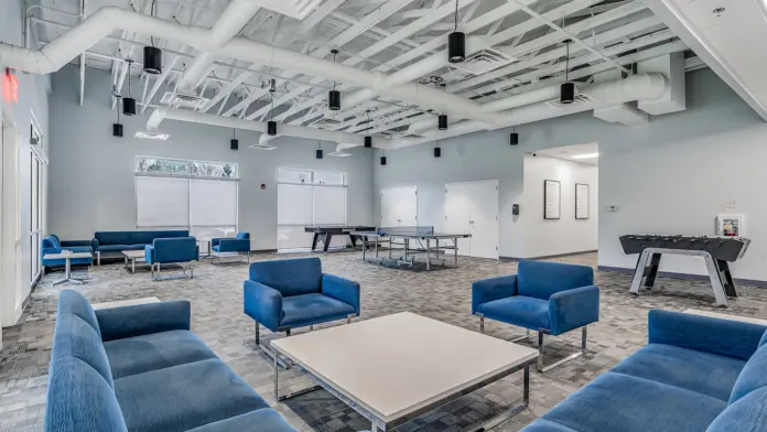 Spacious activity room with blue chairs, a ping pong table, and a foosball table at Boca Recovery Center Huntington.