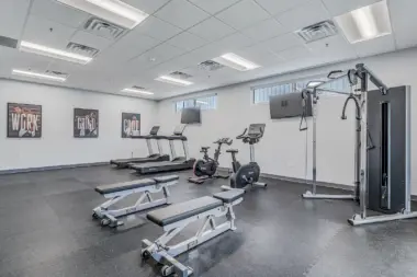 Well-equipped fitness room at Boca Recovery Center Huntington with exercise machines, benches, and motivational posters.