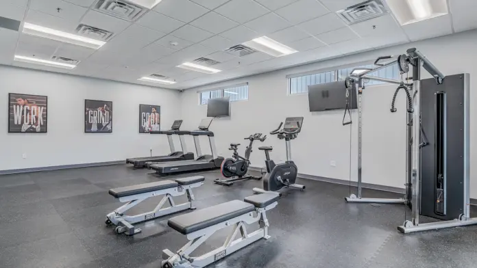 Well-equipped fitness room at Boca Recovery Center Huntington with exercise machines, benches, and motivational posters.