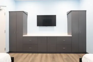 Patient room at Boca Recovery Center Huntington, complete with storage cabinets and a wall-mounted television.