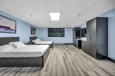 A spacious and modern recovery bedroom with two full-size beds, wood flooring, large wardrobes, a desk, and contemporary wall art, designed for comfort and privacy.