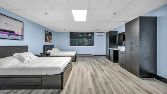 A spacious and modern recovery bedroom with two full-size beds, wood flooring, large wardrobes, a desk, and contemporary wall art, designed for comfort and privacy.