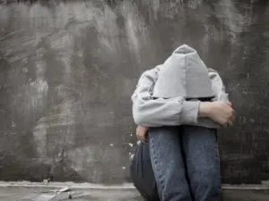 A depressed person in a hoodie clutches their knees