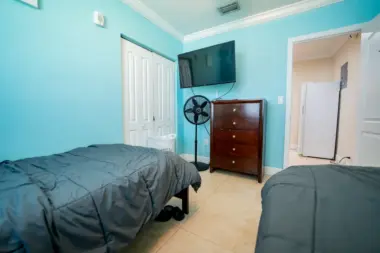 A bedroom at Reign Residential Treatment Center in Southwest Ranches, FL with two beds with blue comforters and a large TV
