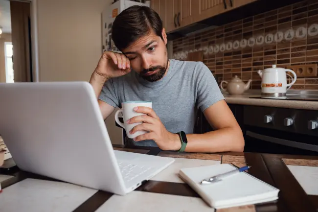 A tired man rubs his eye while holding a cup of coffee