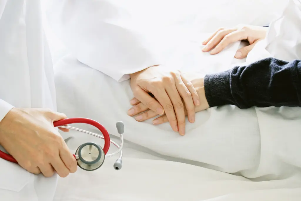 A doctor holds hands with a patient who is off screen