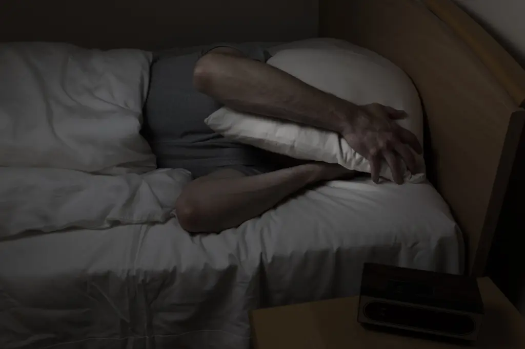 a man covers his face with a pillow, struggling to fall asleep