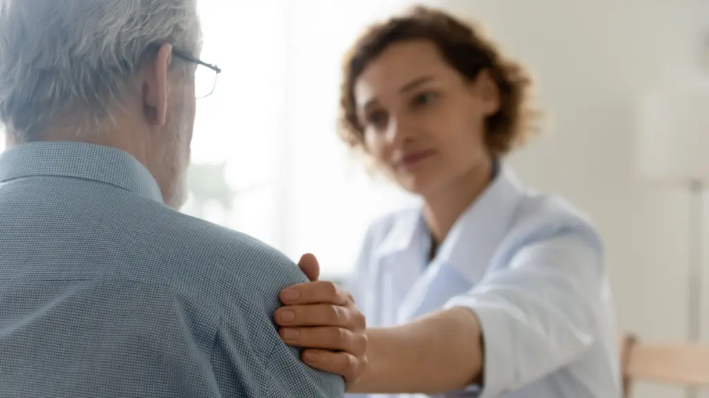 A doctor consoles an elderly patient by placing a hand on their shoulder