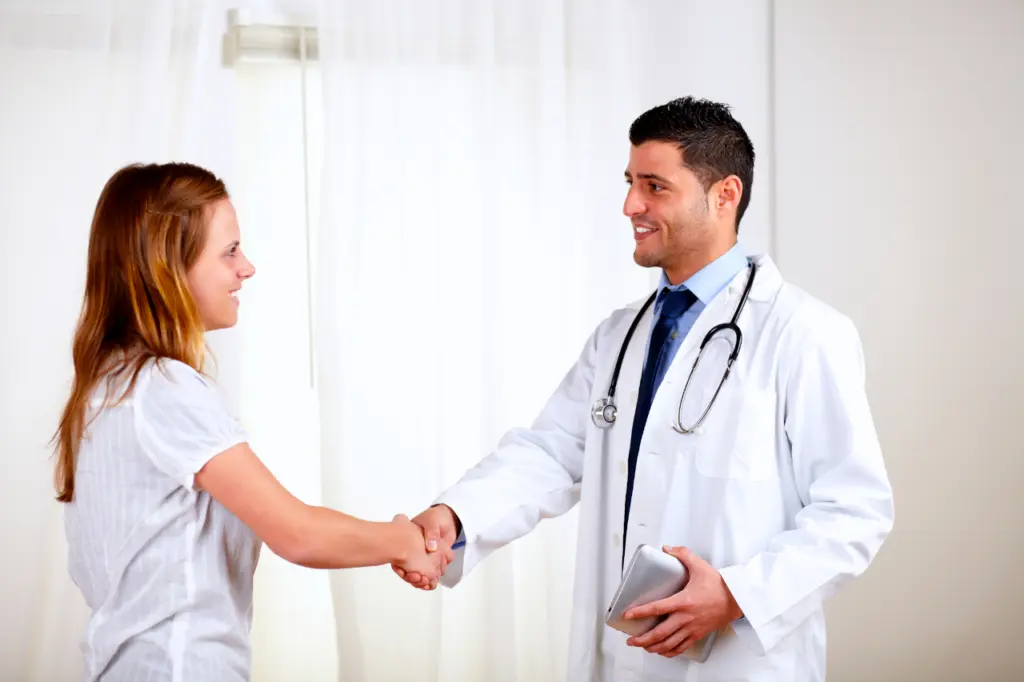 A woman shakes hands with a doctor while they both smile