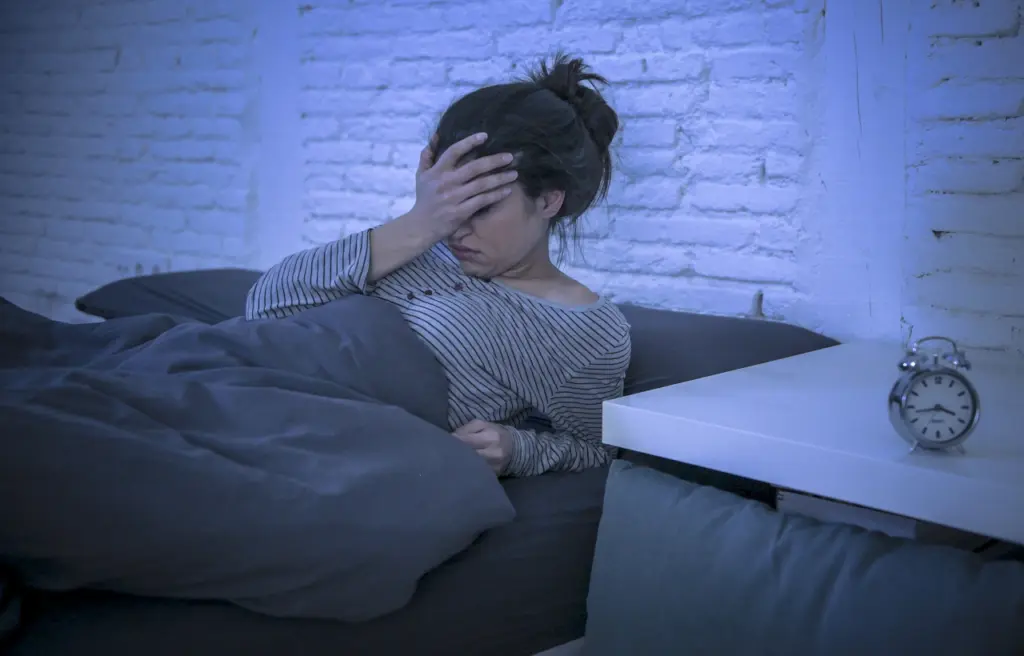 A woman clutches her forehead after struggling to go to sleep