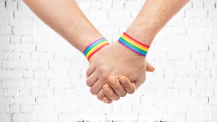 Two people holding hands while wearing rainbow wristbands
