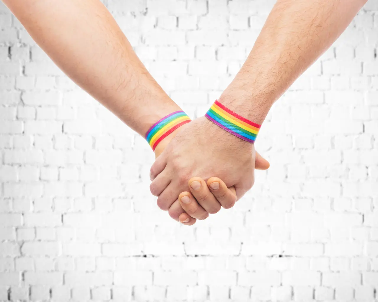 Two people holding hands while wearing rainbow wristbands