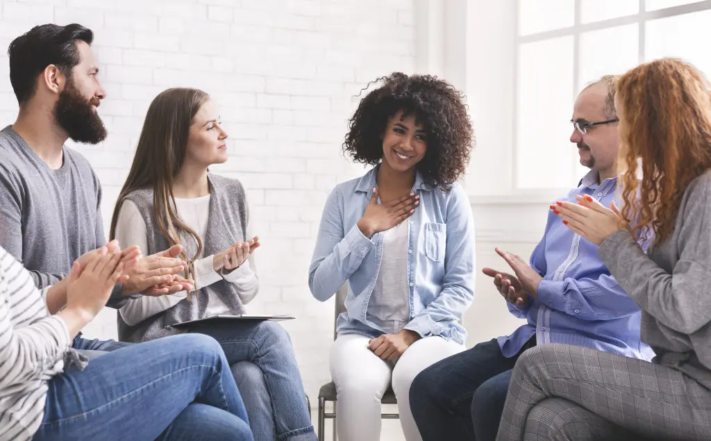 People smile as they participate in a support group meeting, possibly alcoholics anonymous or a similar 12-step group
