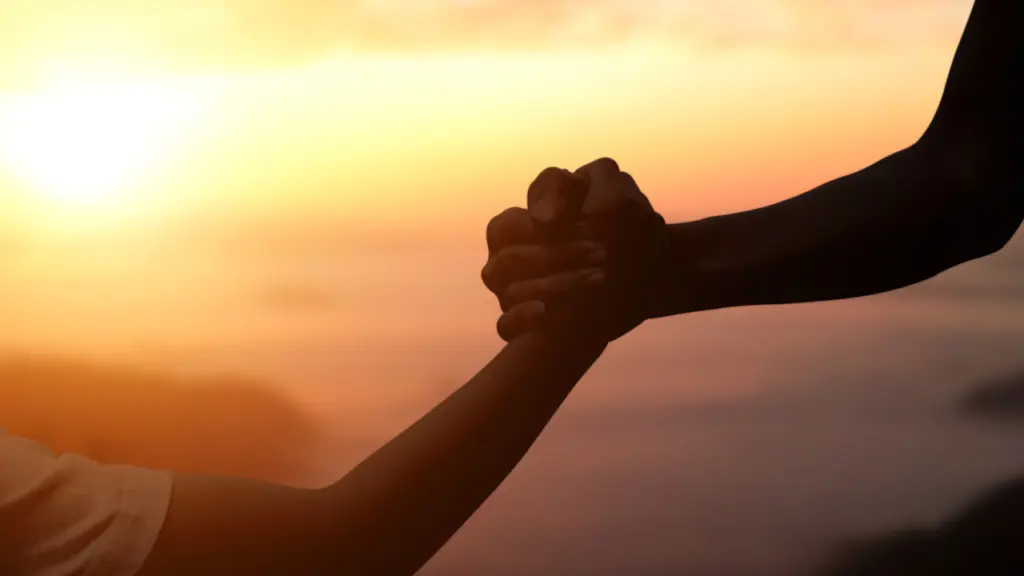 A person helps another person up a hill, two hands gripping together