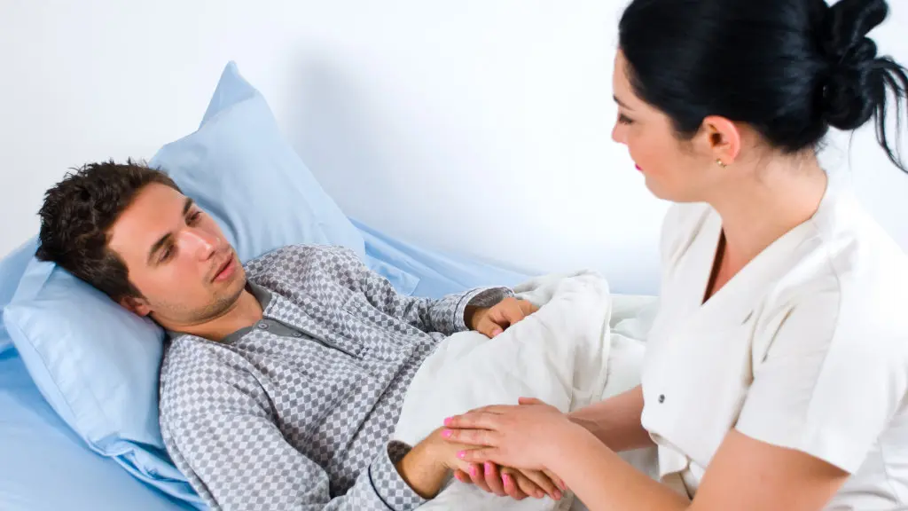 A doctor speaking with a patient as they lie in a hospital bed