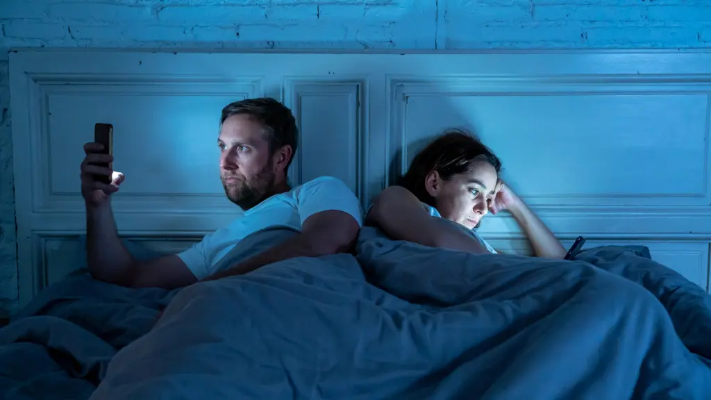 A couple resting in bed, paying attention to their phones instead of each other.