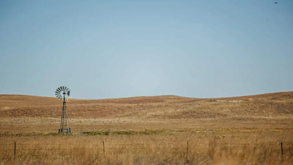 A wide shot of rural plains with a lone windmill standing in the distance