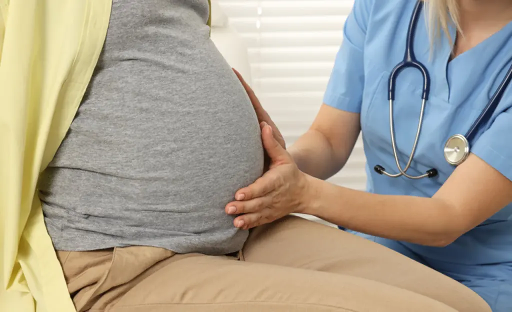 A doctor presses their hands against a woman's pregnant belly. Learn more about rehab for pregnant and postpartum mothers here.