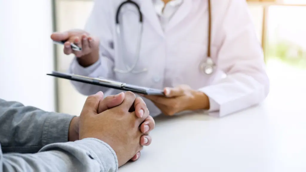 A doctor holding a clipboard with speaking with a patient.