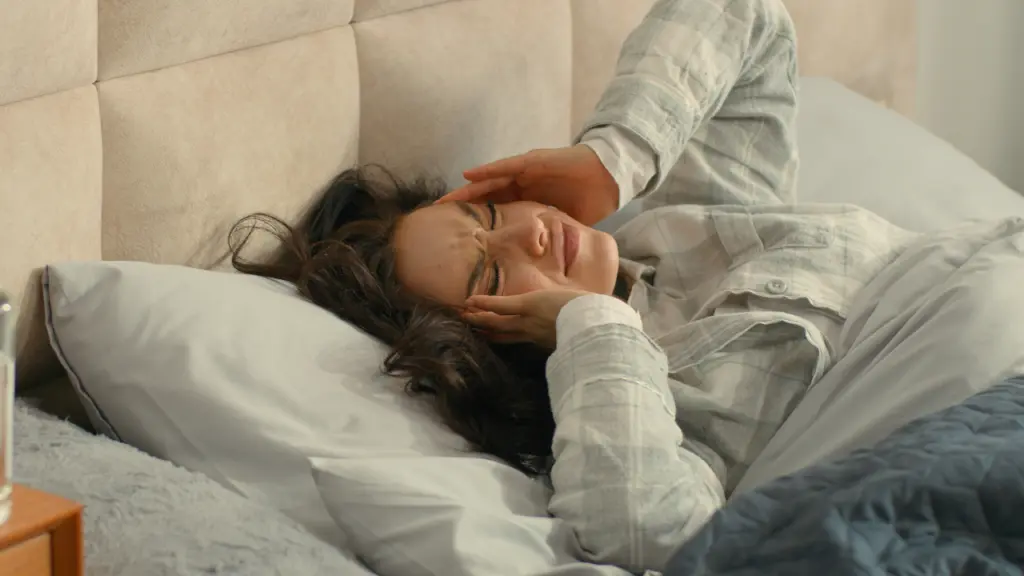 A distressed woman grips her head while lying in bed. Is benzodiazepine withdrawal dangerous? Learn more here.