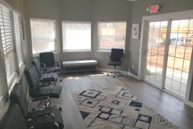 Interior office with multiple windows, black office chairs, bench seating, patterned rug, and glass exterior doors.