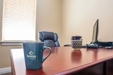 Interior office desk with branded mug, chair, succulent plant, computer monitor, and window.