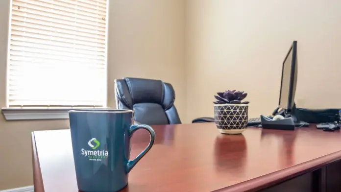 Interior office desk with branded mug, chair, succulent plant, computer monitor, and window.