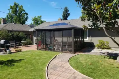 Outdoor patio area featuring screened pavilion, brick pathway, manicured lawn, and seating areas