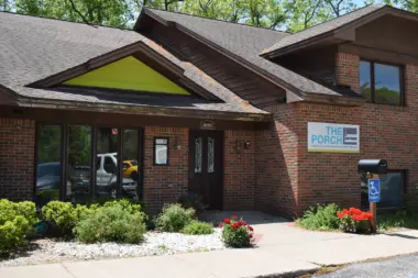 Exterior brick building featuring lime-green triangular roof accent, black doors, and landscaped flower beds